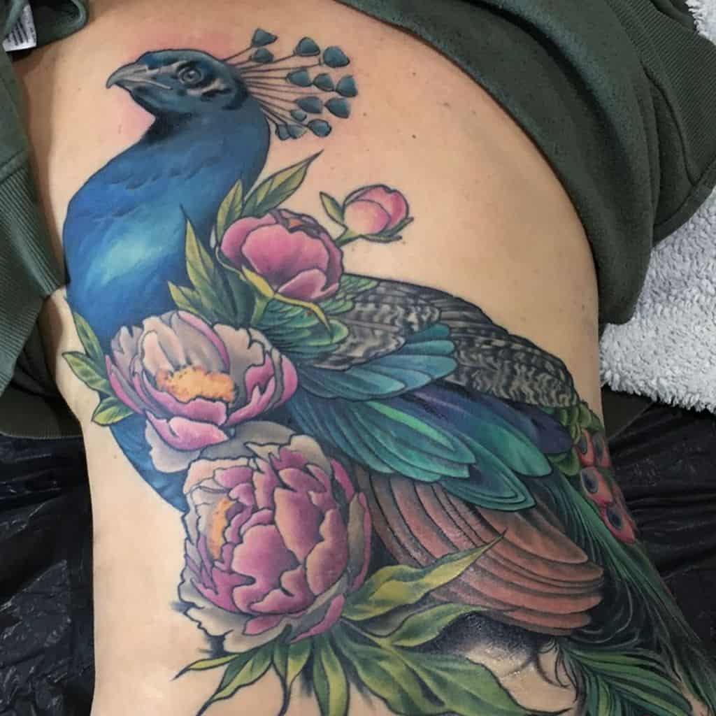 Colorful peacock tattoo with intricate details, featuring vibrant feathers and peonies on the upper arm and side.
