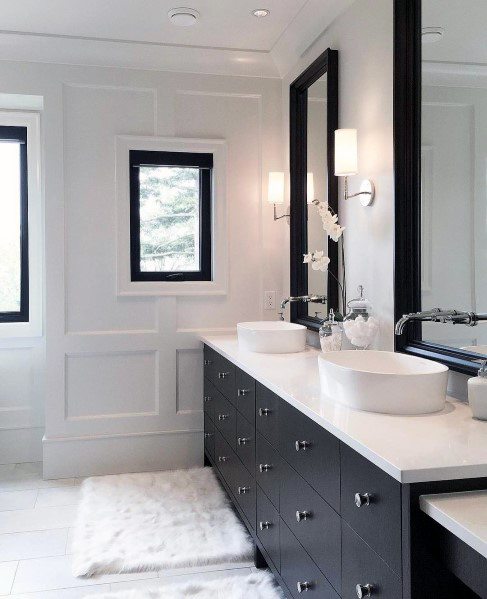 Elegant master bathroom with black vanity, white vessel sinks, and paneled walls.