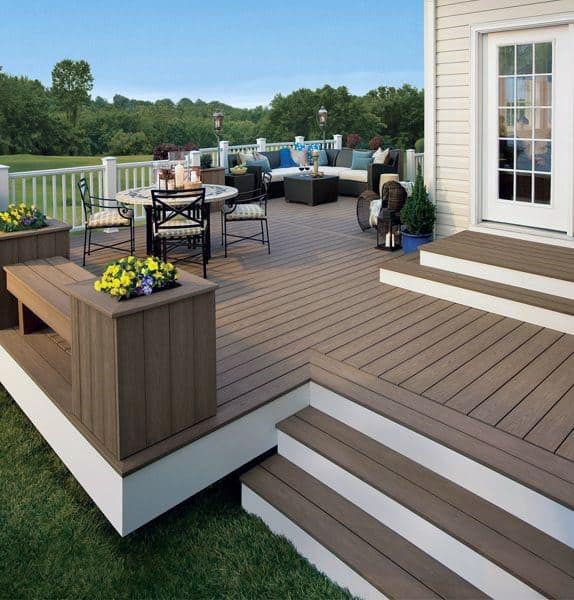 Spacious backyard deck with brown wood flooring, seating, dining area, and garden view.