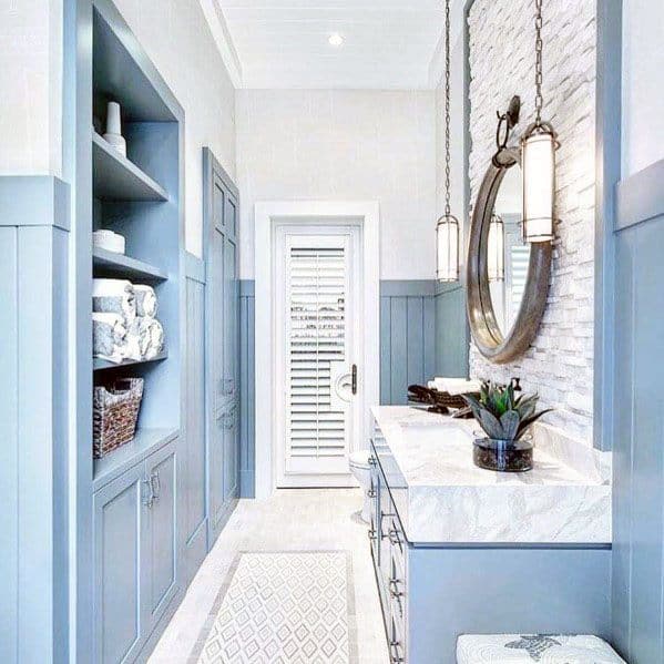 Bathroom with light blue cabinets, white brick accent wall, round mirror, and pendant lights.
