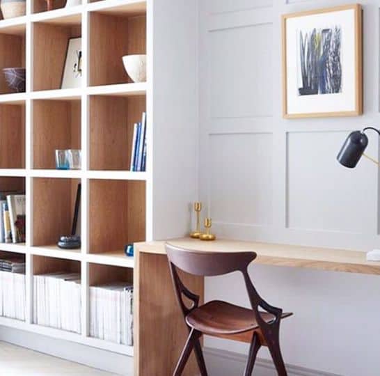 Minimalist home office with built-in wooden desk, modern chair, and a bookshelf filled with books and decor items