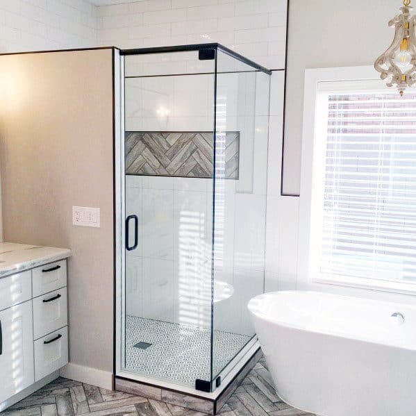 Modern bathroom with a corner glass shower, white freestanding tub, and herringbone tile flooring