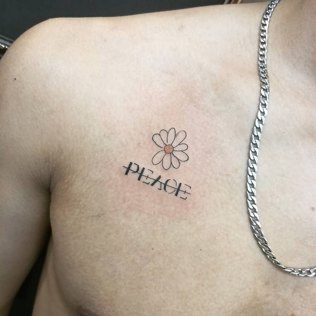 Chest tattoo small cartoon white and yellow daisy above stylized script ‘P E A C E