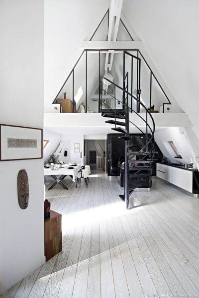 A bright attic loft with whitewashed wooden floors, an A-frame structure, and a sleek black spiral staircase.