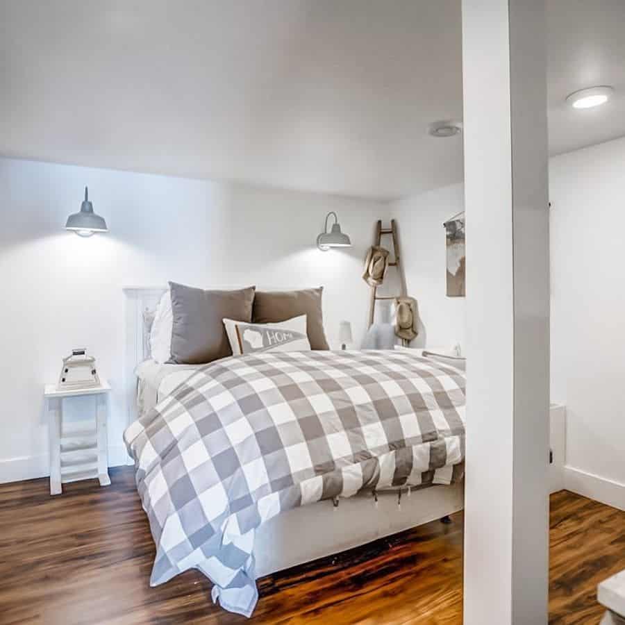 White basement bedroom with plaid bedding, wall sconces, and wooden ladder decor.