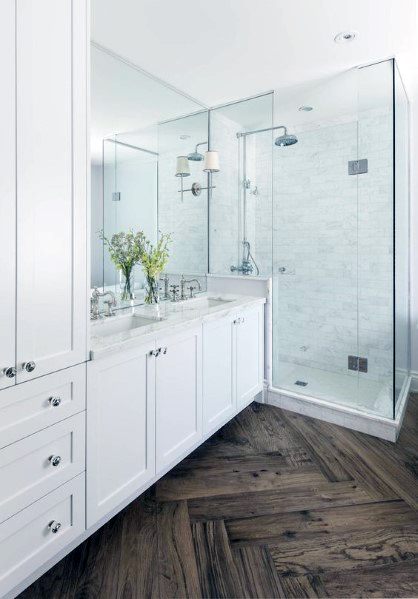 Modern bathroom with glass shower, white cabinets, and elegant herringbone wood floor