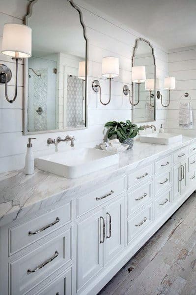 Elegant bathroom with dual white sinks, large mirrors, and sconces on a marble-topped vanity