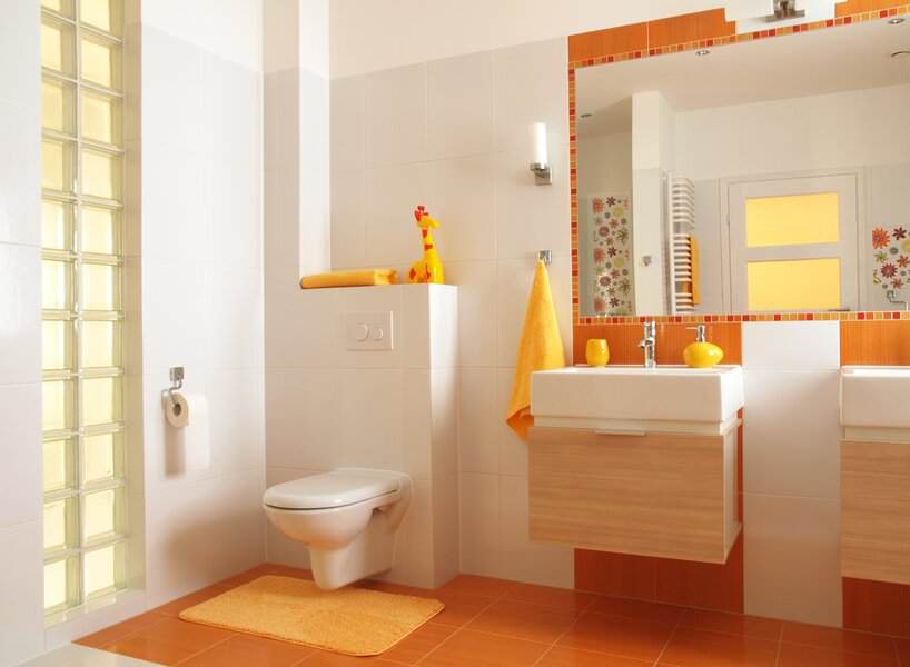 White bathroom featuring orange tile trim, a large mirror, and playful yellow decor elements.