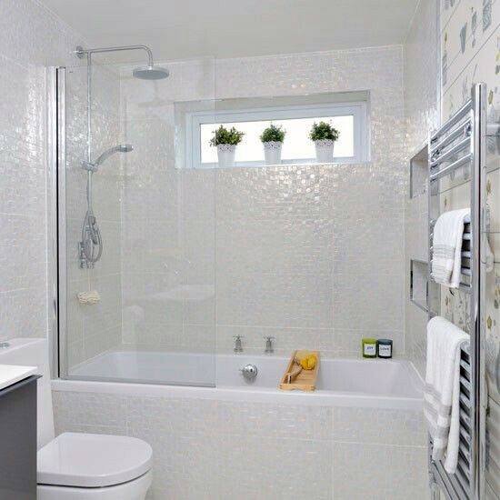 Bright white bathroom with glossy mosaic tiles, bathtub, and small window with potted plants.