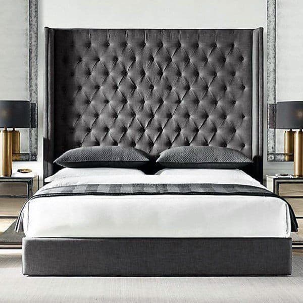 Elegant bedroom with a tall, tufted grey headboard, black lamps, and neatly arranged grey and white bedding