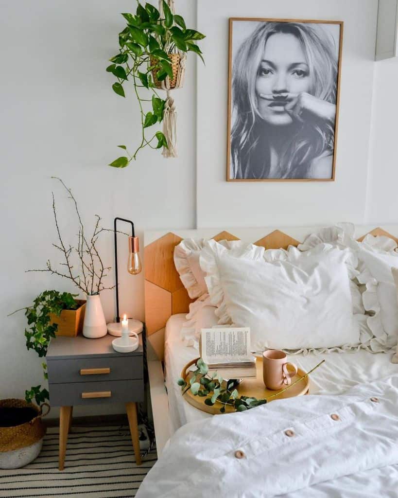 Cozy bedroom with layered bedding, hanging plant, and Kate Moss wall art.