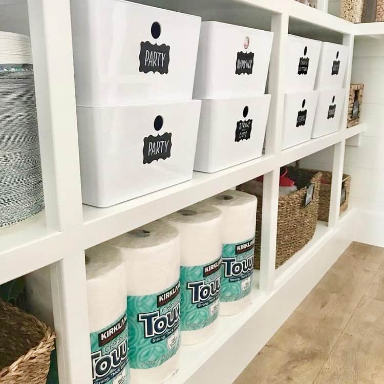 White labeled bins on shelves in a basement storage area with paper towels.