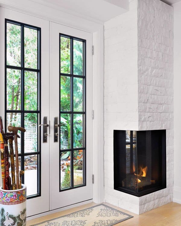 Bright corner with white brick fireplace, glass French doors, and decorative umbrella stand.