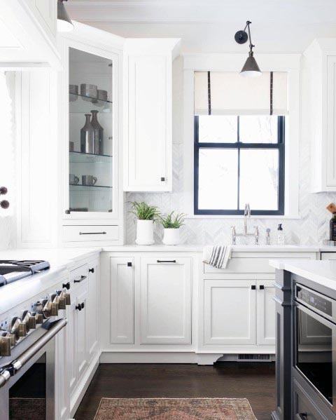 A sleek white kitchen with herringbone tile, open shelving, and dark wooden floors.
