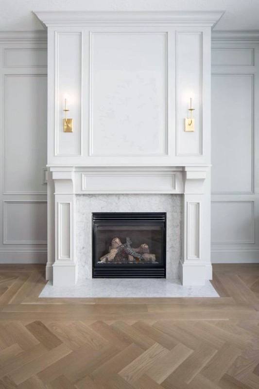 White paneled fireplace with a marble surround, decorative mantel, and gold wall sconces.