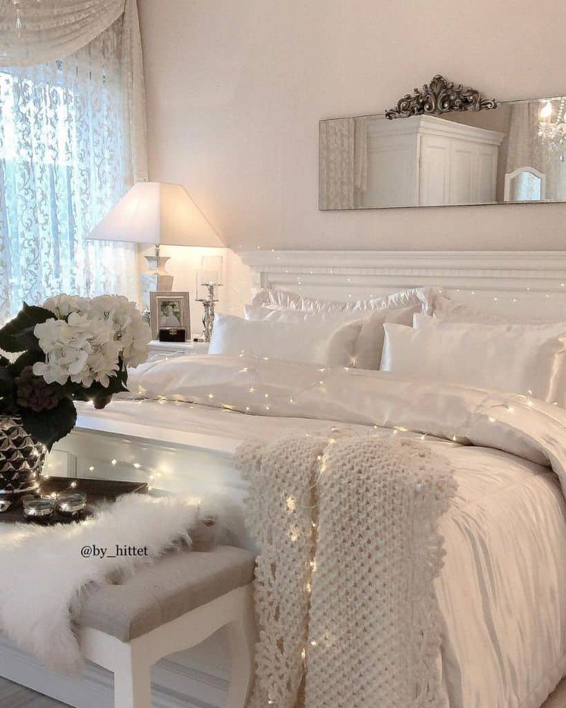 Cozy bedroom with a white bed, soft pillows, a knit throw, and soft lighting, featuring elegant decor and flowers