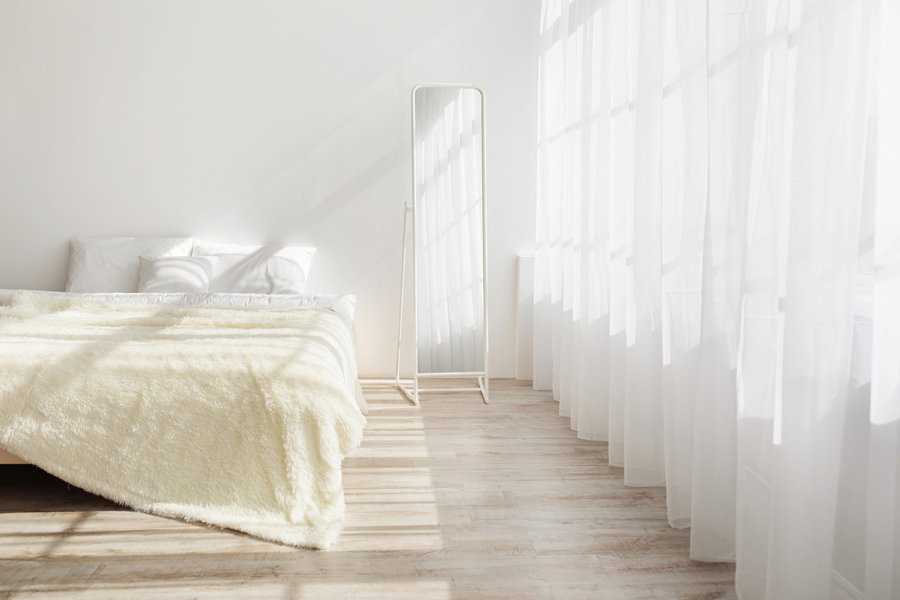 Bright minimalist bedroom with sheer white curtains and a floor-length mirror.