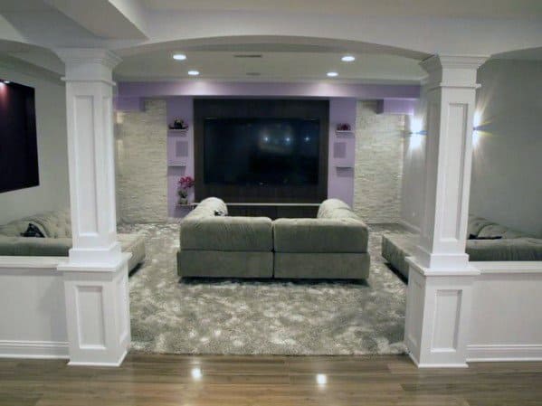 Basement lounge with white decorative poles, large TV, and plush gray seating area.