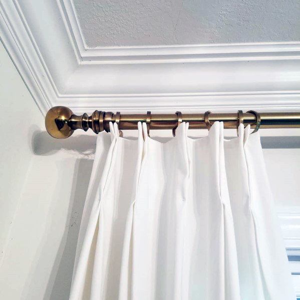 Stylish crown molding paired with a brass curtain rod and white drapes, creating a clean and elegant design for the room