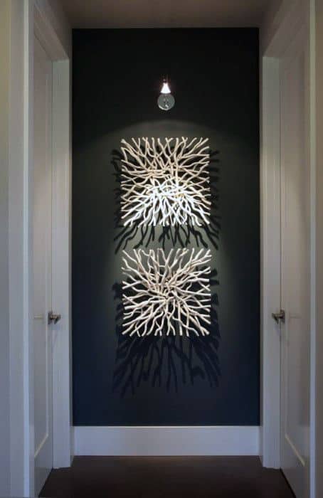 Two square white driftwood wall art pieces with spotlight illumination in a dark hallway.