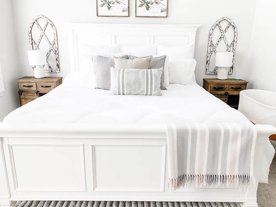 Farmhouse-style bedroom with a white bed, striped throw pillows, wooden side tables, lamps, and wall decor