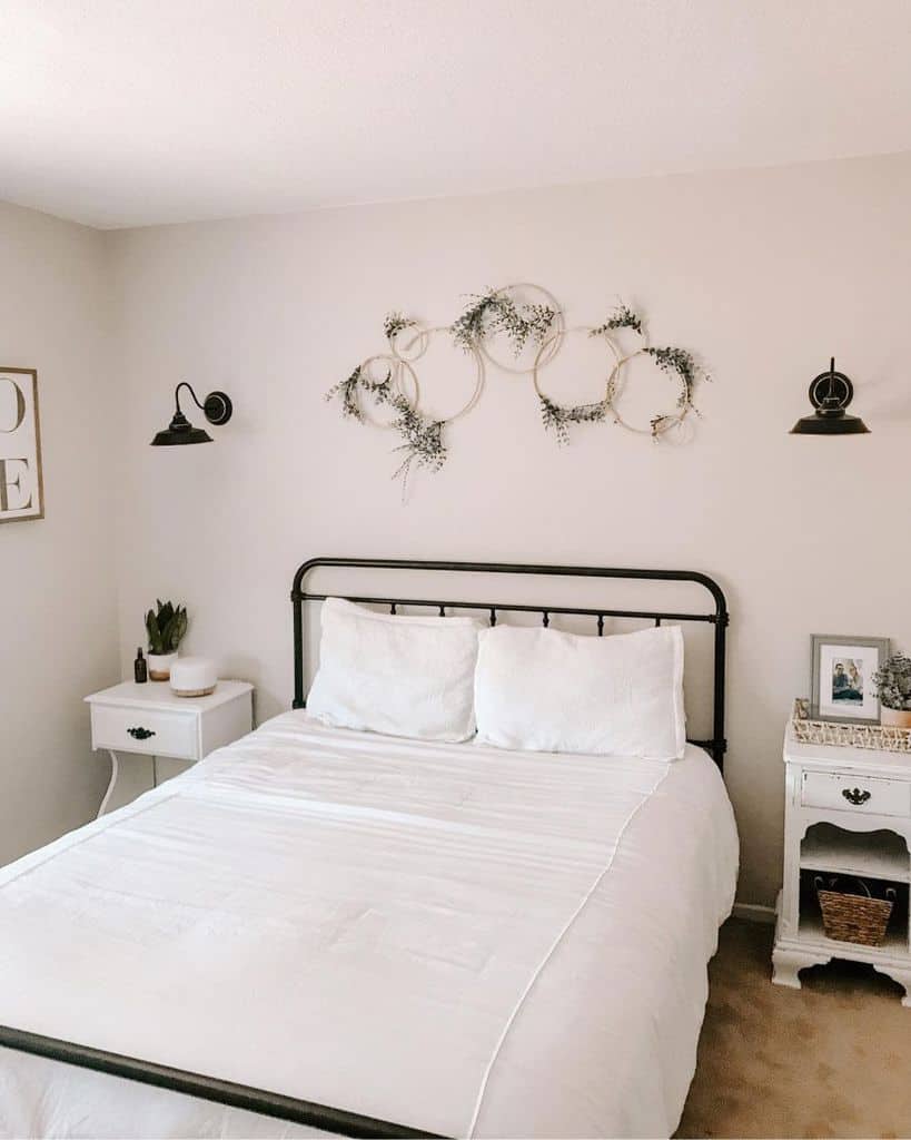 Minimalist farmhouse bedroom with white bedding, metal bed frame, circular wreaths decor, and two bedside tables