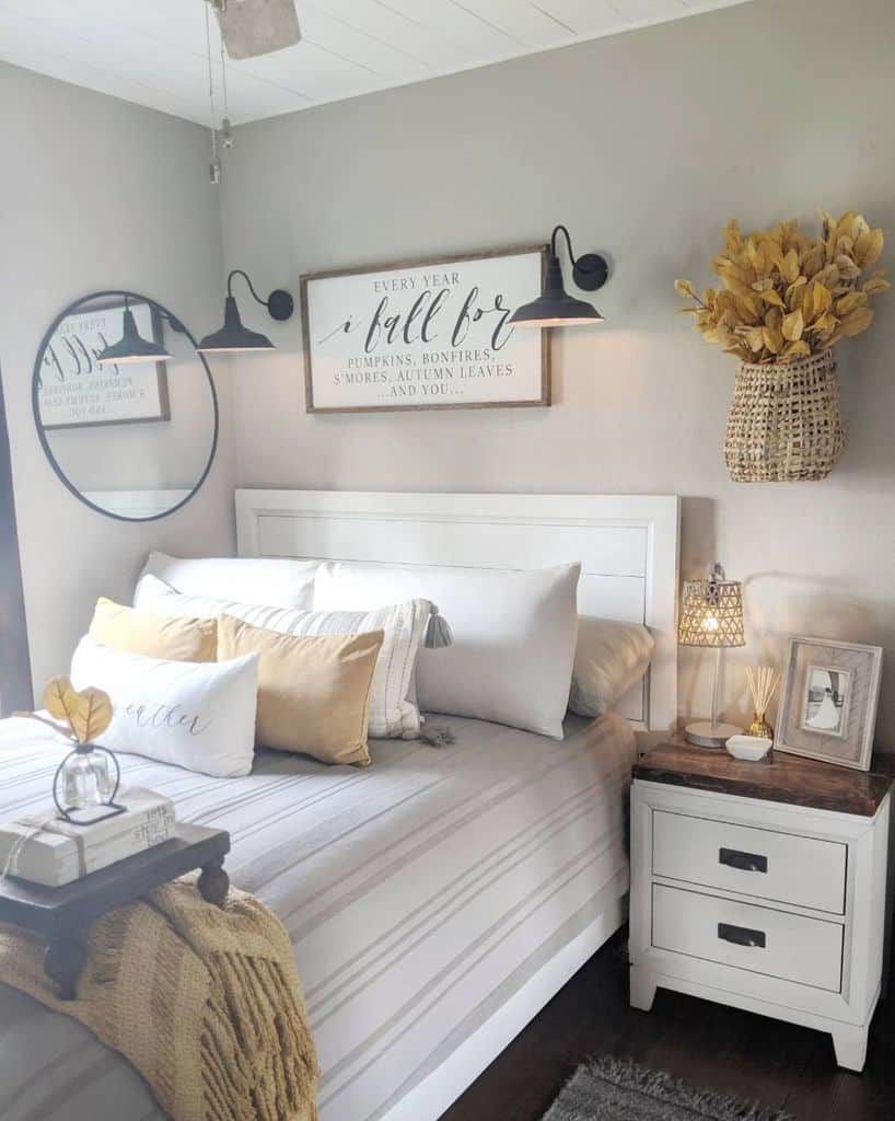 Cozy farmhouse bedroom with a striped bed, decorative pillows, round mirror, wall art, and vase of yellow flowers