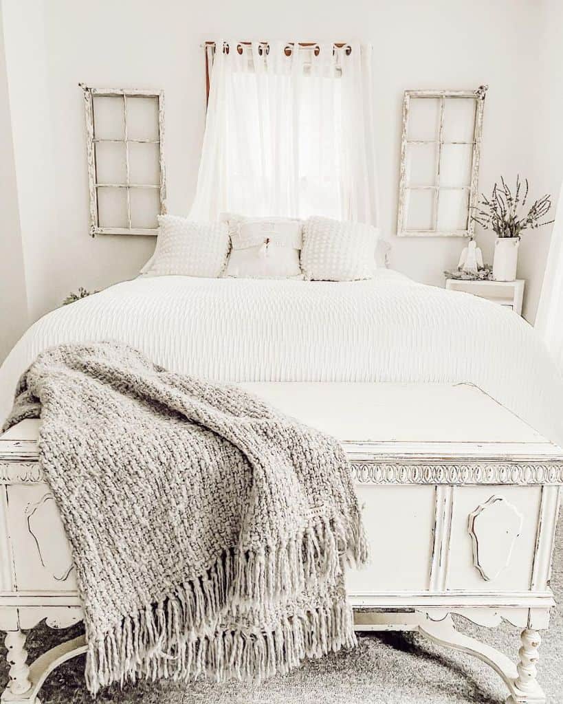 Cozy farmhouse bedroom with a white bed, knitted throw blanket, vintage decor, and light curtains filtering soft light