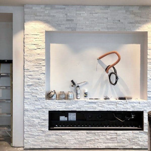 Unfinished wall with stacked stone, incomplete wiring, and tools on a recessed shelf space