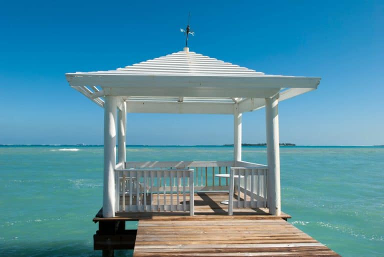 A white gazebo on a pier stretches over a turquoise ocean under a clear blue sky