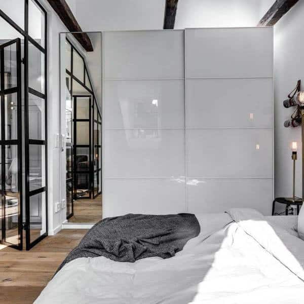 A modern bedroom with sleek white high-gloss sliding closet doors and a minimalist design, featuring clean lines and a spacious look
