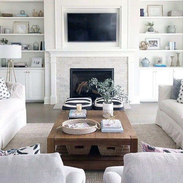 Classic living room with a central fireplace framed by built-in white bookcases. The design includes cabinets, open shelving with decor accents, and a wooden coffee table that adds warmth to the neutral color palett