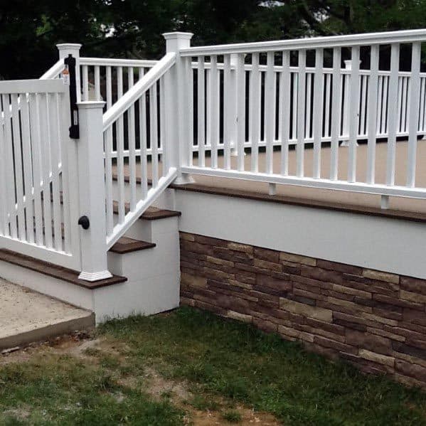 White railing on steps with stone siding and greenery, leading to a charming gate
