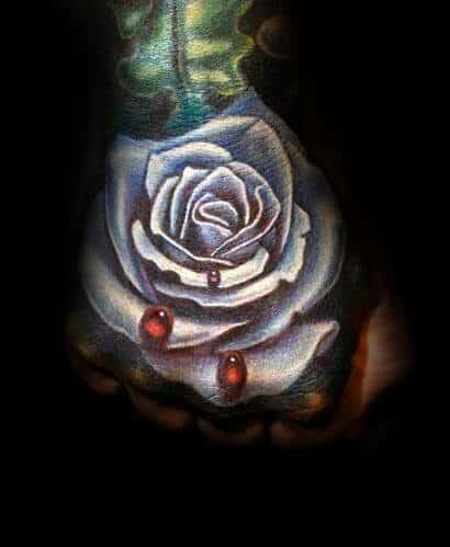 A white rose tattoo with red droplets on a hand