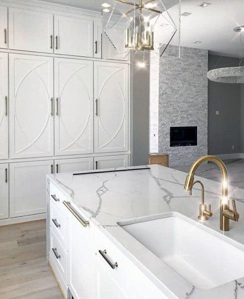 White kitchen with gold faucet, marble countertops, and custom cabinet design.