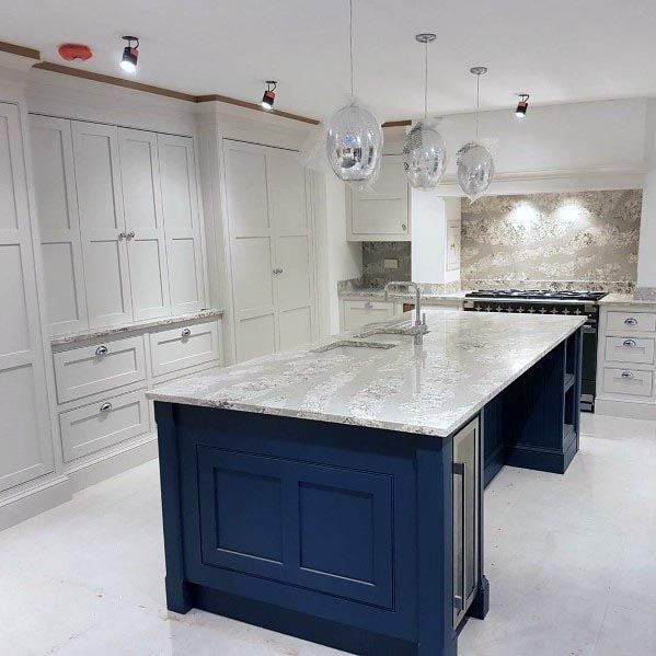 White kitchen with navy blue island, marble countertops, and glass pendant lights.