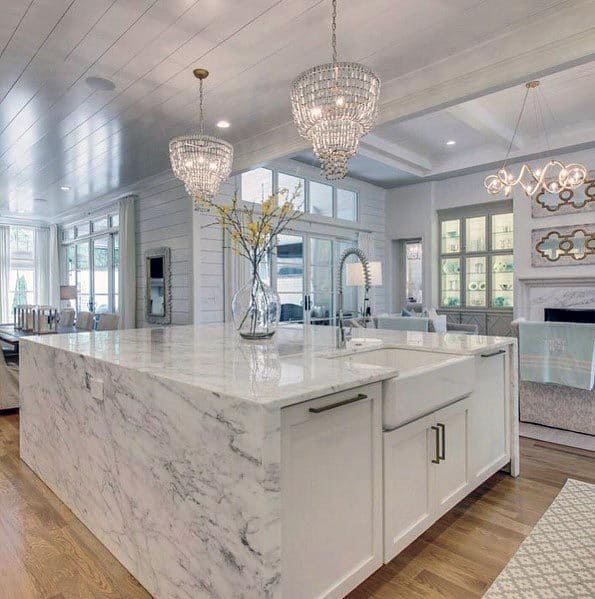 A luxurious marble island, farmhouse sink, and crystal pendant lights in a cozy, open kitchen.