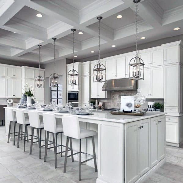 Spacious white kitchen with large island, white bar stools, and hanging pendant lights.