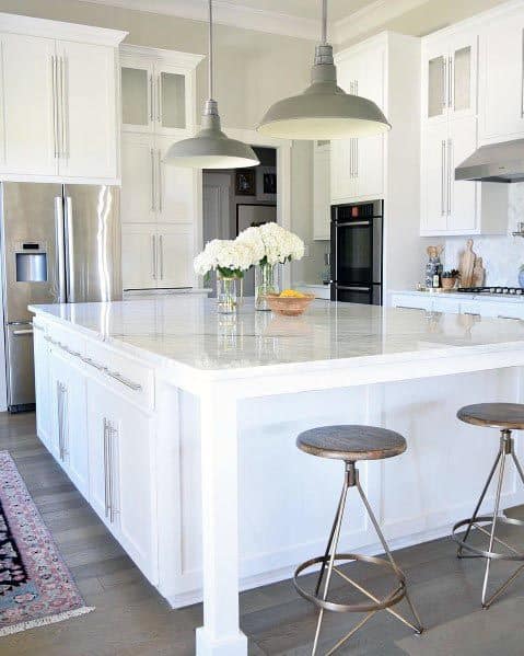 White kitchen with large island, rustic bar stools, and pendant lights.
