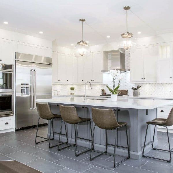 Modern white kitchen featuring a clean stone backsplash and a large island with gray base cabinets. Sleek stainless steel appliances, pendant lighting, and stylish bar stools complete the airy and sophisticated look.