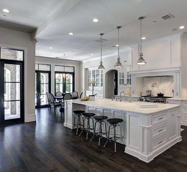 White kitchen with dark hardwood flooring, marble island, and black bar stools.