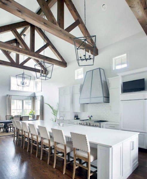 White kitchen with vaulted ceiling, exposed wooden beams, and a long island with bar stools.