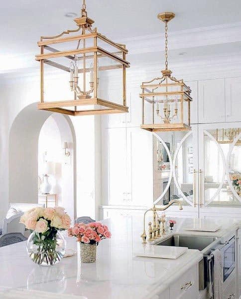 White kitchen with gold pendant lights, marble island, and fresh floral arrangements.