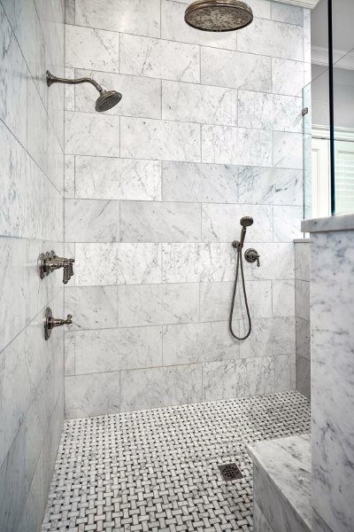 White marble shower with rainfall showerhead and woven-pattern tile floor design.