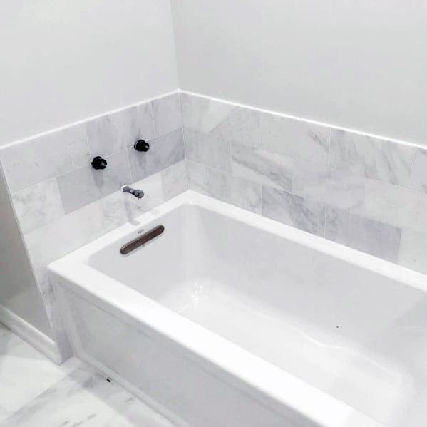 White bathtub with marble tile surround and minimalist black fixtures.