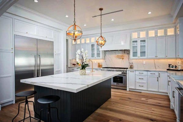 Luxurious kitchen with a white marble backsplash and matching countertop on the spacious island. The dark island base contrasts elegantly with the warm wood flooring and brass-accented pendant lights, creating a timeless and sophisticated ambiance.