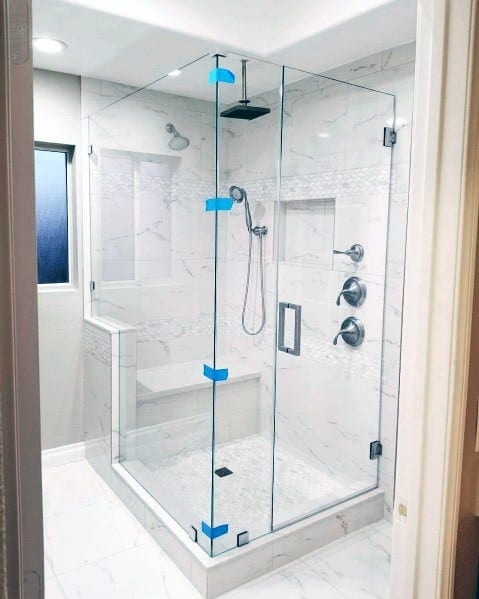 A modern corner glass shower enclosure with marble-tiled walls, a rainfall showerhead, and a built-in bench