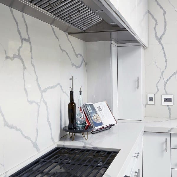 Modern kitchen with white marble slab backsplash, gas stovetop, and sleek white cabinets.