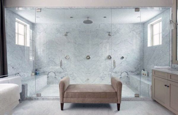 Spacious marble shower featuring dual showerheads and a central rain shower, flanked by a beige bench