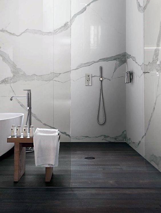 Modern shower with white marble walls, dark wood flooring, and minimalist fixtures.
